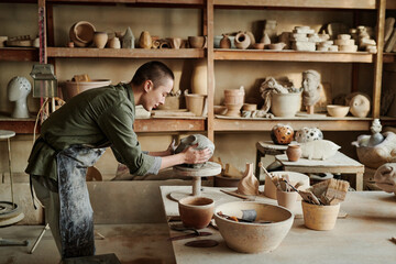 Female sculptor using equipment she holding clay with hands and making form of vase