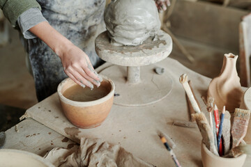 Close-up of woman putting hands in bowl with water and making vase from clay on the equipment