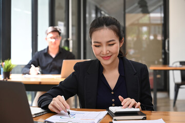 Smiling businesswoman using calculator and checking financial reports.