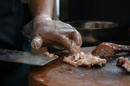 Close up of chef slicing roasted chicken on wooden cutting board. Chef preparing grilled chicken. Dicing chicken meat.