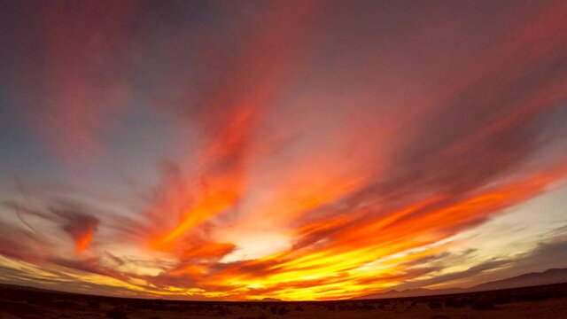 Colorful swirling clouds in the predawn sky followed by a golden sunrise over the Mojave Desert wilderness - wide angle time lapse