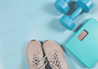flat lay of grey sneakers ,digital weight scale, blue dumbbells on blue background. healthy lifestyle and weight loss concept.