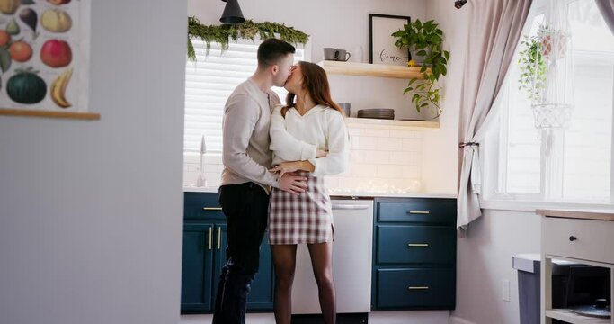 Romantic couple hugs, smiles and kisses in a bright kitchen while dancing, wide angle.