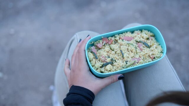 Over-the-shoulder shot of girl opening lunch box and eating outdoors