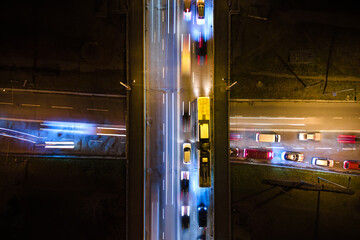 Aerial view of road intersection with fast moving heavy traffic at night. Top view of urban transportation. Rush hour with motion blurr car trail lights