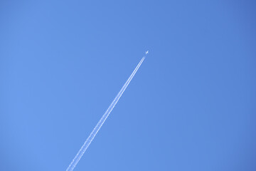 Distant passenger jet plane flying on high altitude on clear blue sky leaving white smoke trace of contrail behind. Air transportation concept