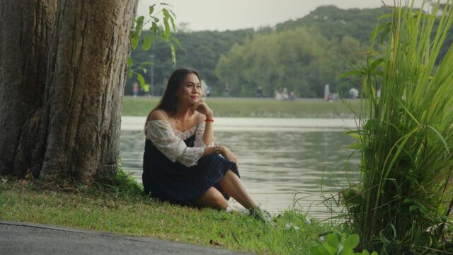 Transgender Asian woman leaning against a tree in the park enjoying the moment.