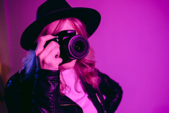 Portrait of a beautiful girl photographer in a hat who takes pictures in the studio on a fiolet background