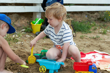 Two children play in the sand with plastic toys