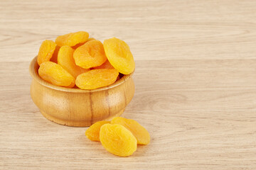 Wooden plate filled with dried apricots on a wooden background, next to scattered dried apricots
