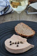 Morceau de foie gras avec des baies et une tartine de pain dans une assiette à côté d'un verre de vin blanc