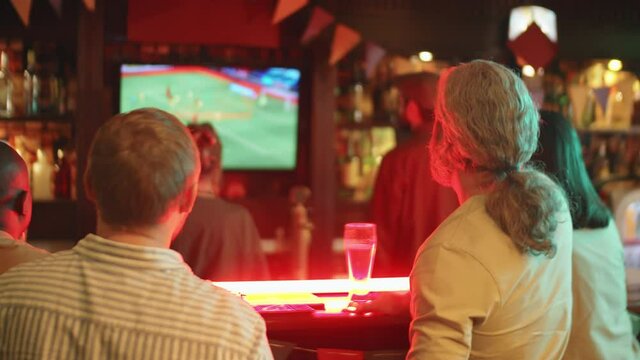 Back view shot footage of unrecognizable men and women enjoying watching football match in pub