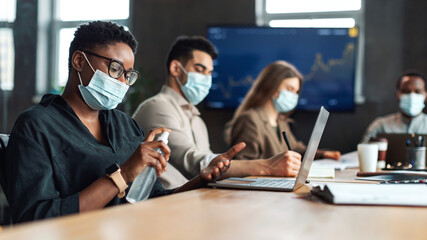 Multicultural workers wearing medical masks, black woman using sanitizer
