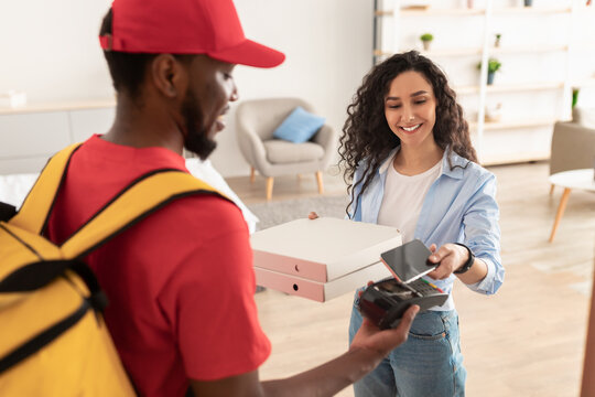 Smiling deliveryman holding POS machine, woman paying with phone