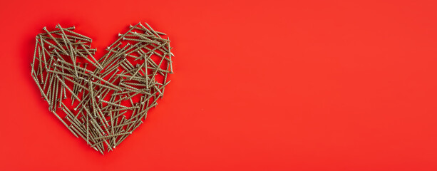 Small metal nails laid out randomly in shape of heart on red background. Broken heart relation...