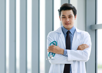 Fototapeta premium Professional Asian physician man in formal business uniform of clinical hygiene gown smiling and standing with arm crossed and medical stethoscope in hand as confident on career expertise