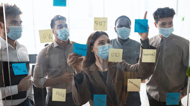 Colleagues in face masks brainstorming using post-it notes on wall