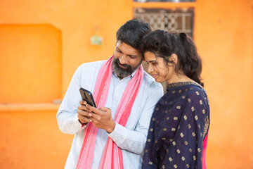 Happy Smiling Traditional Indian rural father and his young daughter using smart phone to make online payment, shopping on internet with cellphone secure banking service system concept.