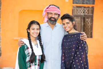 Portrait of happy traditional Indian father with his two young beautiful daughters showing his love and support, small family, rural india. beard Man with cloth on head smiling with girls.