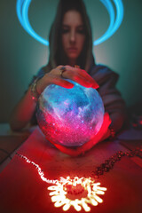 Predictable Caucasian woman with globe planet in her hands and luminous pictogram on the table. Astrology applied magic and mysticism. Focus on the texture of the ball. Clairvoyant out of focus - obrazy, fototapety, plakaty