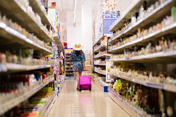 Shelves full of products in a shop with a woman walking around with a suitcase