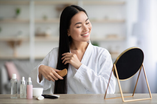 Cheerful asian lady combing hair with wooden brush