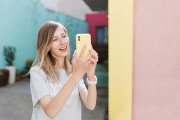 Pretty laughing caucasian woman with smartphone has good time outdoor. portrait of trendy millennial girl with blonde hair wears fashionable clothing