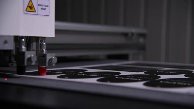 An industrial advertising plotter close-up cuts a template on the cardboard packaging for products. shallow depth of field in real time. Live camera