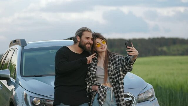 Positive couple taking selfie near car among green field