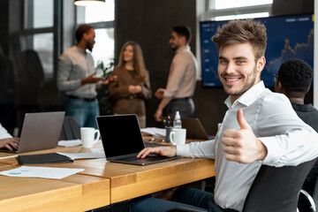 Confident businessman sitting at desk showing thumbs up gesture