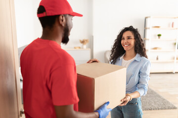 Black delivery man giving box to woman standing at door
