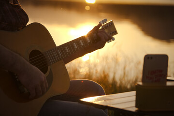 Man playing guitar at sunset lake, Close-up male hand playing on acoustic guitar outdoor with...