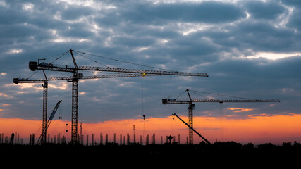 Silhouette of tower crane and large buildings construction site at sunset in evening time. New construction site with cranes on sunset background.