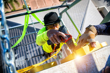 Obraz na płótnie Canvas A high-rise maintenance worker uses a drilling tool on a crane.