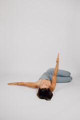 Brunette is engaged in sports. Young woman performs exercise from yoga or fitness, she lies on her...