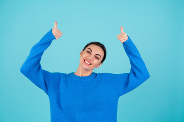 Beauty portrait of a young woman in a blue knitted sweater and natural day makeup, smiling cheerfully and pointing her finger up to an empty space