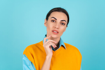 Young woman in a shirt and an orange vest on a turquoise background looks thoughtfully at the camera