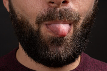 Obraz premium Cropped photo closeup of funny man grimacing at camera with sticking out his tongue isolated over black background.
