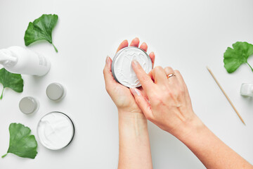 Woman applying  cosmetic moisturizing hand cream. Cosmetic products, green leaves on white table....