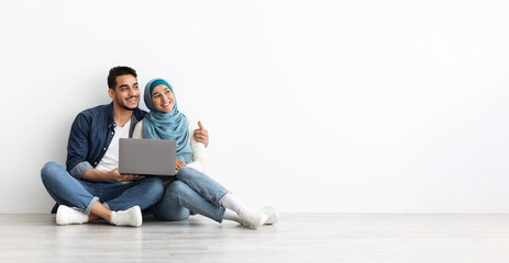 Happy family sitting on floor with laptop in empty room