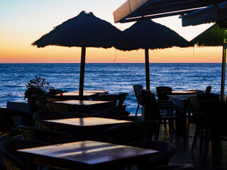 Sillas y mesas de un restaurante frente al mar en el atardecer