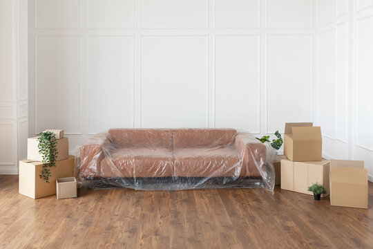 Empty living room with couch, stacks of boxes during relocation - a couch covered in plastic