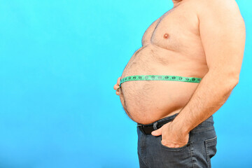 A fat and pot-bellied man with a large belly measures his waist with a centimeter.