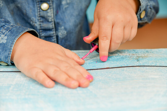 Little girl paints her nails with her mother's nail polish.