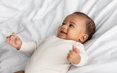 Cute little African American infant lying in bed and laughing
