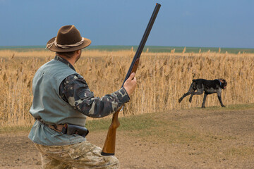 Hunter man in camouflage with a gun during the hunt in search of wild birds or game. Autumn hunting season.