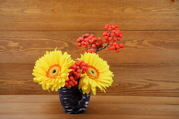 Beautiful yellow gerbera flower. Standing in a black vase. Red mountain ash on a branch. Close-up. still-life. On a wooden background. (chamomile) Holiday concept. For a postcard. Space for text.