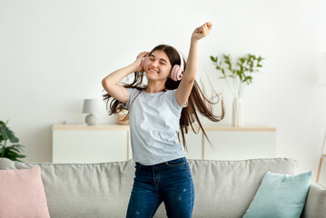 Happy Indian teenage girl with headphones dancing to beautiful music at home