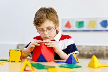 Little kid boy with glasses playing with lolorful plastic elements kit in school or preschool...