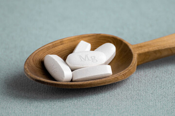 Tablets , vitamins with the abbreviation Mg ( magnesia, the macronutrient magnesium ) lying in a wooden spoon on a light background. Copy space. - obrazy, fototapety, plakaty